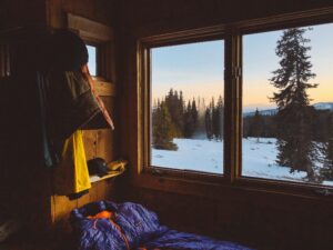 View from inside a cabin in the winter overlooking snow covered forest at sunrise